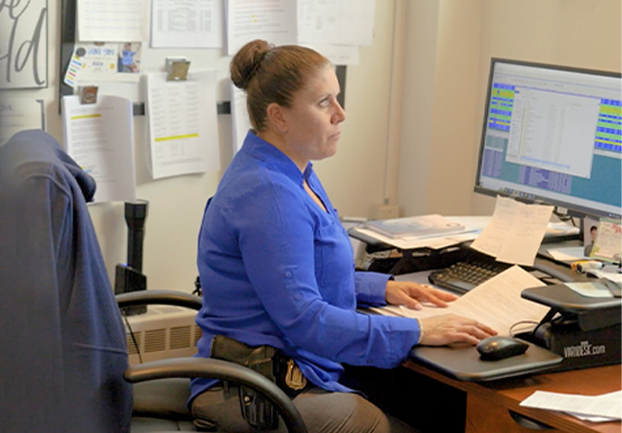 Woman working at a desk with paperwork and a computer monitor in an office