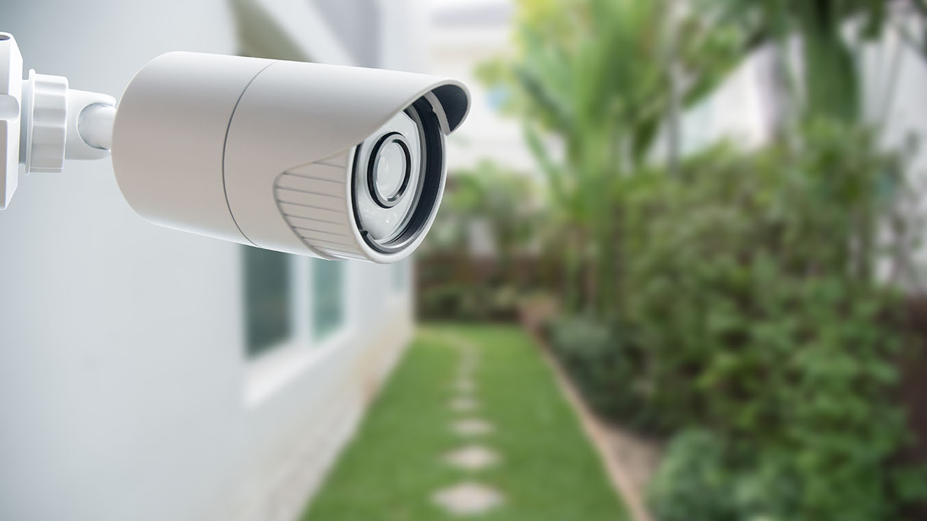 White outdoor security camera mounted on a house outside