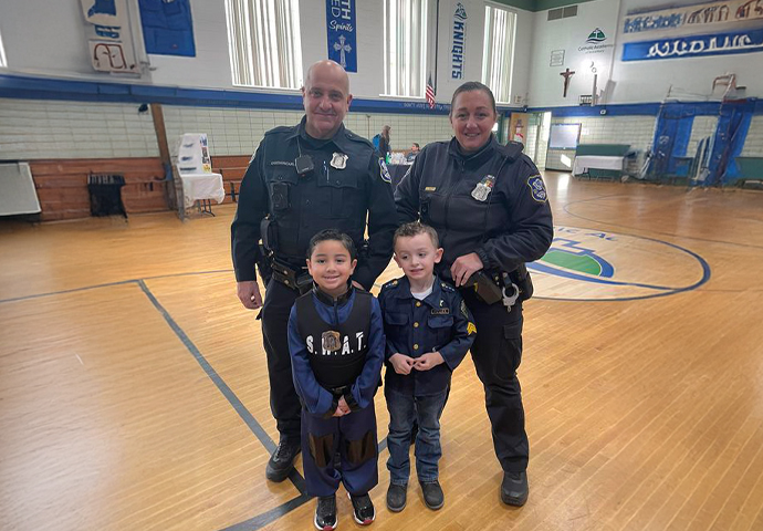Two Waterbury police officers standing with two young boys in police and SWAT uniforms in a gymnasium