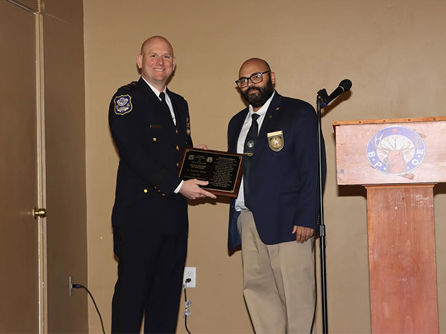 Waterbury Police Captain receiving a commemorative plaque from a man in a business jacket at an indoor event