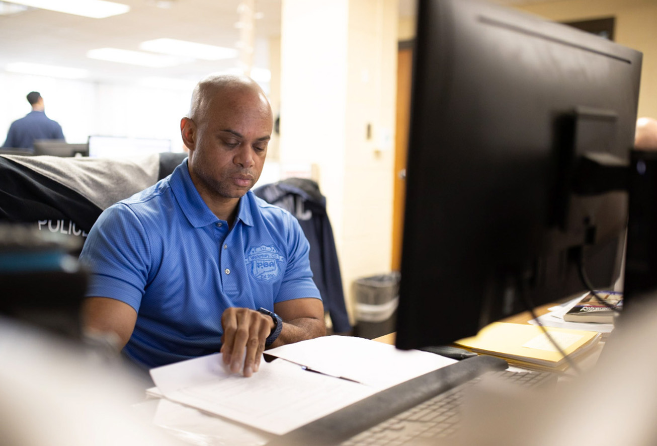A Waterbury police department staff member reviewing documents at a desk in an office