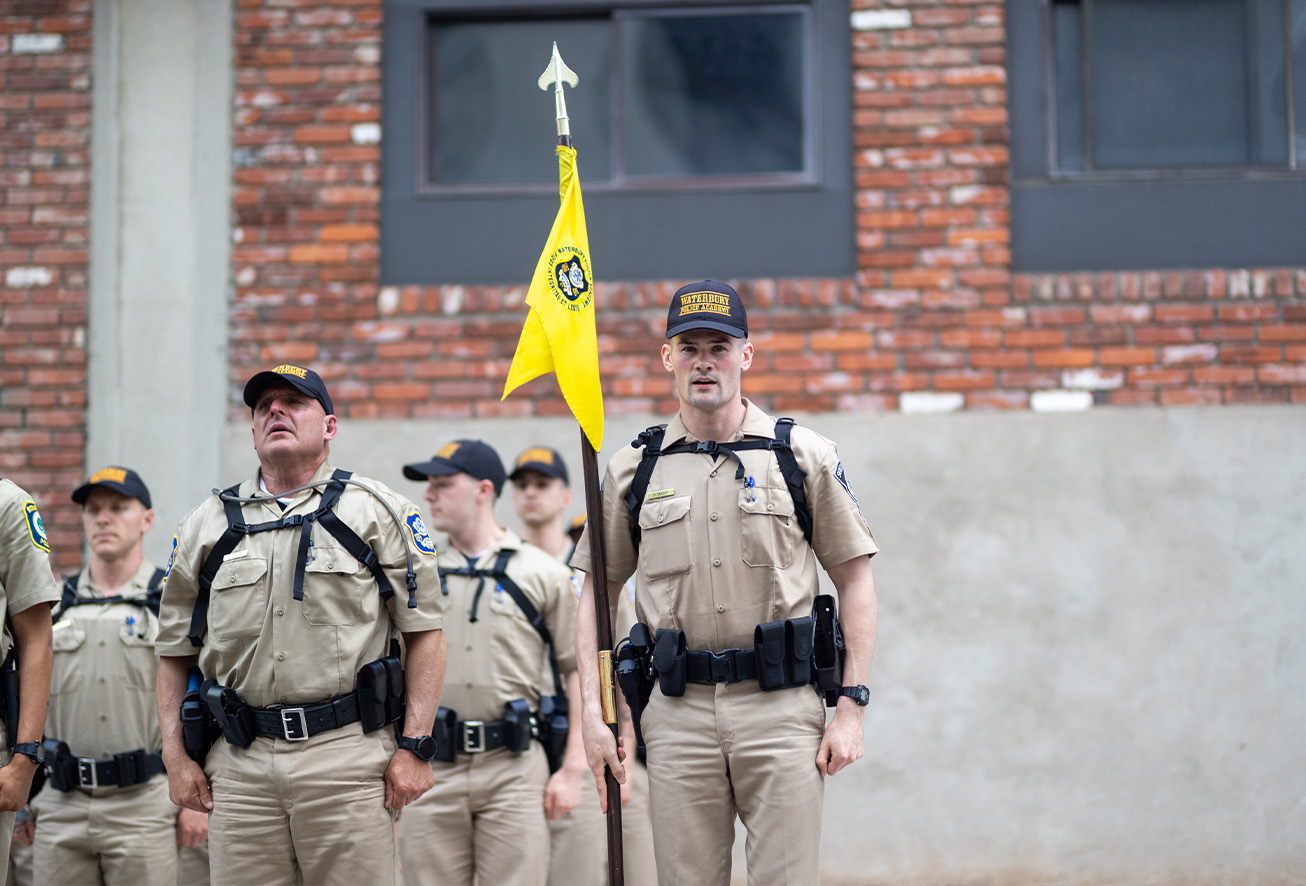 Group of Waterbury Police officers in tactical gear holding a yellow flag outdoors