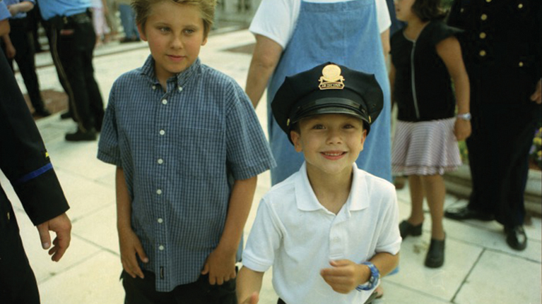 Two kids smiling, one wearing a police cap that is too big for him