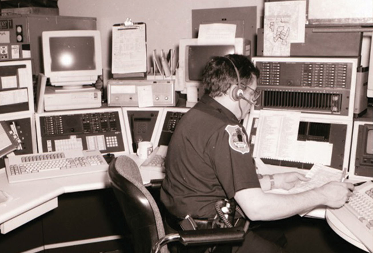 A vintage photo of a Waterbury police dispatcher working in the communication center surrounded by old monitors