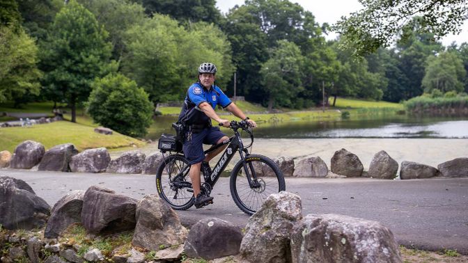 Waterbury police officer on a mountain bike near a pond in a park